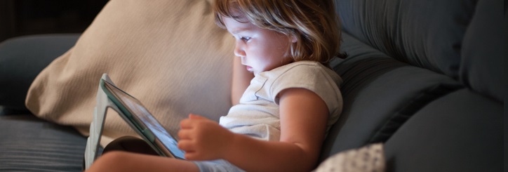 little child sitting comfortably in sofa watching tablet