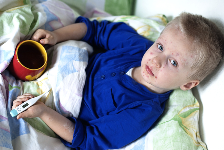 Boy with measles in bed with tea and a digital thermometer