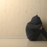 Suffering child with face hidden, sitting in a dark room