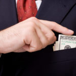 Man in suit putting $100's in boutonniere close up.