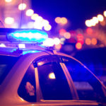 Blue light flasher atop of a police car. City lights on the background.