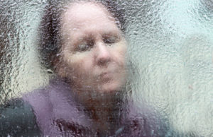 close up of a woman with a sad expression, gazing through a window covered in thick ice 
