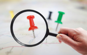 Magnifying glass looking at closeup of push pin tacks in a map