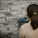 little girl facing a wall, holding her stuffed bear