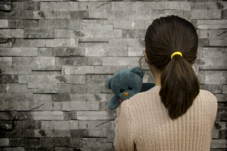 little girl facing a wall, holding her stuffed bear