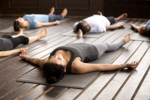 Group of young people practicing yoga, lying in Corpse pose or Savasana.