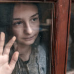 Emotional portrait of a teenage girl looking out window