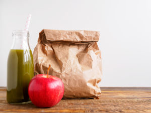 Brown bag lunch with green drink and apple