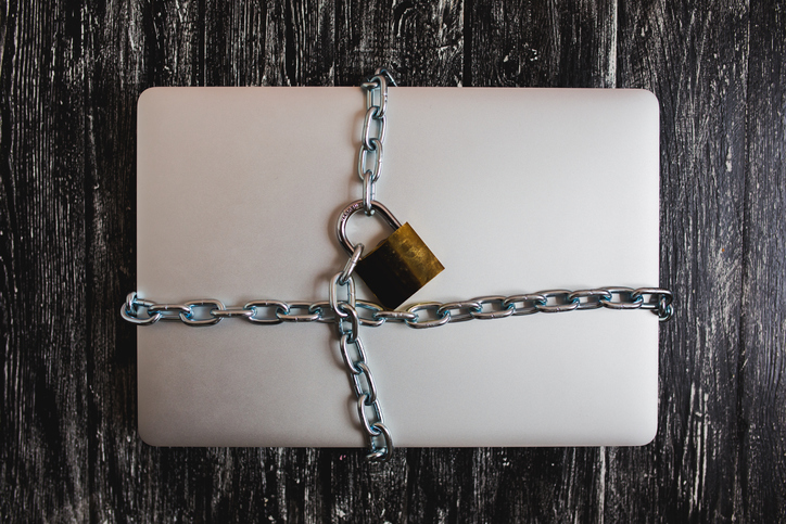 Heavy with a padlock around a laptop isolated on grey table.