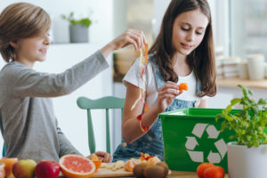 Girl and boy trowing fruits waste into green recycling or composting container