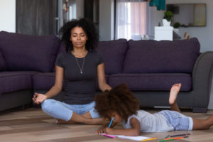 Calm african american mom doing yoga in living room with child daughter