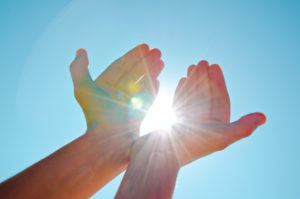 Hands holding the sun with the blue sky background.