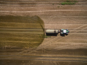 aerial view of a tractor with a trailer fertilizes a freshly plowed agriculural field with manure