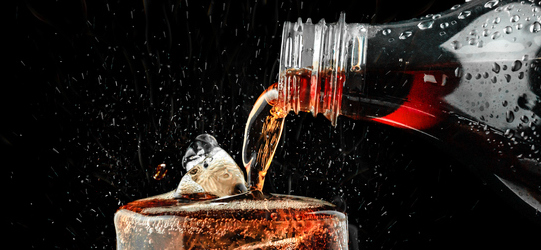 Pour cola in glass with ice splash on dark background.