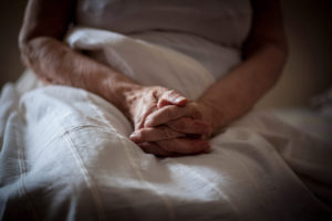 Old woman sitting on bed, close up of hands.